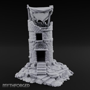 Puede incluir: Una torre de piedra en miniatura de color gris claro con una sección superior en ruinas, un toldo de tela drapeada, una ventana cuadrada, una puerta arqueada con detalle de celosía y escalones de piedra hacia la entrada, sobre una base rocosa.