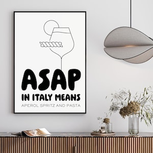 Puede incluir: Impresión artística enmarcada en negro con fondo blanco. La impresión presenta una ilustración de copa de cóctel con una rodaja de limón y el texto "ASAP IN ITALY MEANS APEROL SPRITZ AND PASTA."