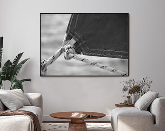 May include: Black and white photograph of a sailboat detail. The image focuses on a section of the sail, rope, and knot. The sail is dark, with a zig-zag stitched edge. The rope is white with black flecks, tied in a knot.