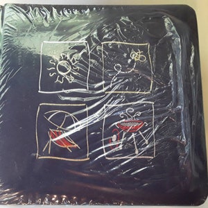 May include: A black photo album with a plastic cover. The cover has four gold squares with illustrations of a sun, a bee, a beach umbrella, and a grill.