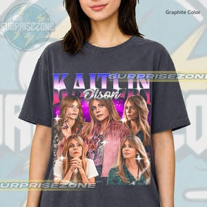 Może przedstawiać: Grafitowa koszulka z retro wzorem przedstawiającym imię Kaitlin Olson i kilka jej zdjęć. Projekt ma fioletowo-różowe tło z tekstem "SURPRISEZONE" w okrągłym wzorze.