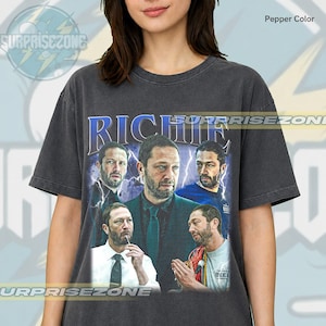 May include: Pepper color t-shirt featuring a collage of images of a man with the name "RICHIE" in blue text. The shirt has a vintage look with the "SURPRISEZONE" logo in the upper left corner.
