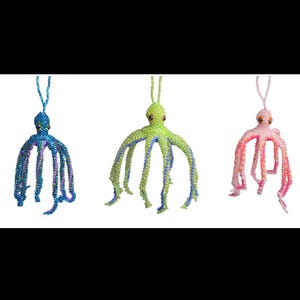 Puede incluir: Tres colgantes de pulpo con cuentas en azul, verde y rosa. El pulpo azul tiene detalles morados, el verde tiene azul y el rosa tiene naranja. Cada pulpo tiene ocho largos tentáculos con cuentas y un lazo para colgar.