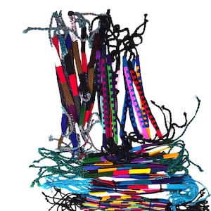 May include: A collection of colorful woven friendship bracelets. The bracelets feature various patterns and colors, including red, blue, green, and purple. Each bracelet has knotted ends.