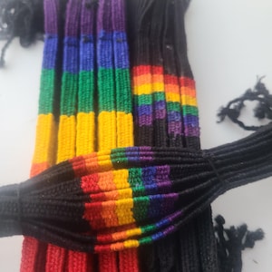 May include: A close-up of a bundle of rainbow colored friendship bracelets. The bracelets are made of woven string and have a black string woven through them.