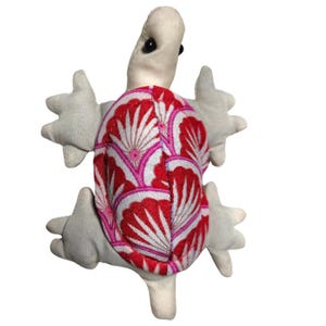 May include: A small, handmade stuffed turtle toy with a white body and a red, white, and pink patterned shell.