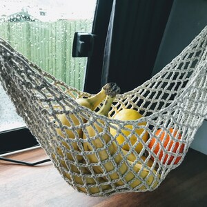 May include: A white crocheted hammock hanging from the ceiling of a vehicle, filled with bananas and oranges.