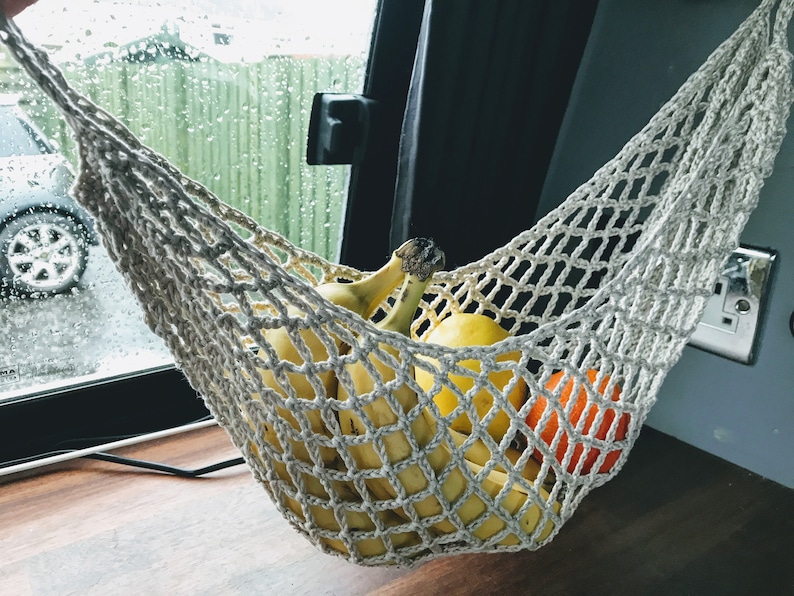 May include: A white crocheted hammock hanging from the ceiling of a vehicle, filled with bananas and oranges.