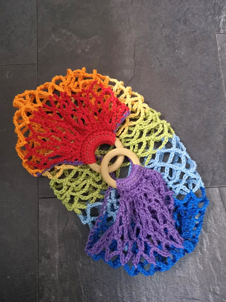 May include: A rainbow crochet bag with wooden handles. The bag is made of a variety of colors, including red, orange, yellow, green, blue, and purple.