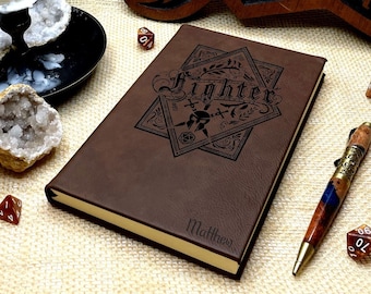 May include: Brown leather journal with a gold-colored edge and a black engraved design of a sword and dice with the word "Fighter" above it. The journal is personalized with the name "Matthew".
