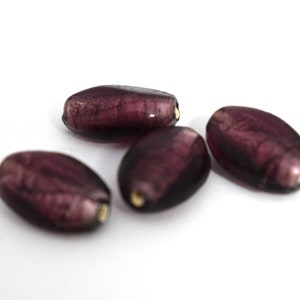 May include: Four purple glass beads with a metallic sheen. The beads are oval shaped and have a slightly irregular surface.