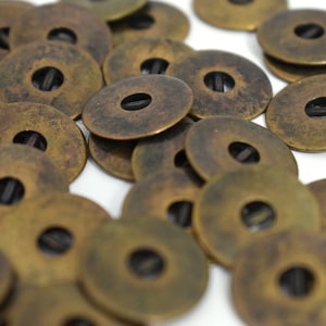 May include: A collection of antique brass-colored metal washers with a central hole. The washers have a slightly tarnished appearance, suggesting age or a vintage aesthetic. The circular design and aged finish give them a rustic appeal, suitable for various craft projects.