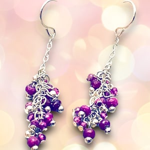 May include: A pair of silver dangle earrings featuring a cluster of purple gemstones. The earrings are crafted with a delicate chain and have a hook fastening.