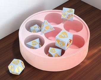 May include: A set of light blue dice with gold numbers and heart symbols, displayed in a pink circular container. The dice are in various shapes, including cubes and a dodecahedron. The container has multiple circular compartments.