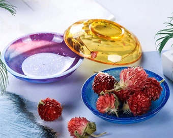 May include: Three small, round, resin dishes in different colors. The dishes are filled with dried flowers. The dishes are on a white surface.
