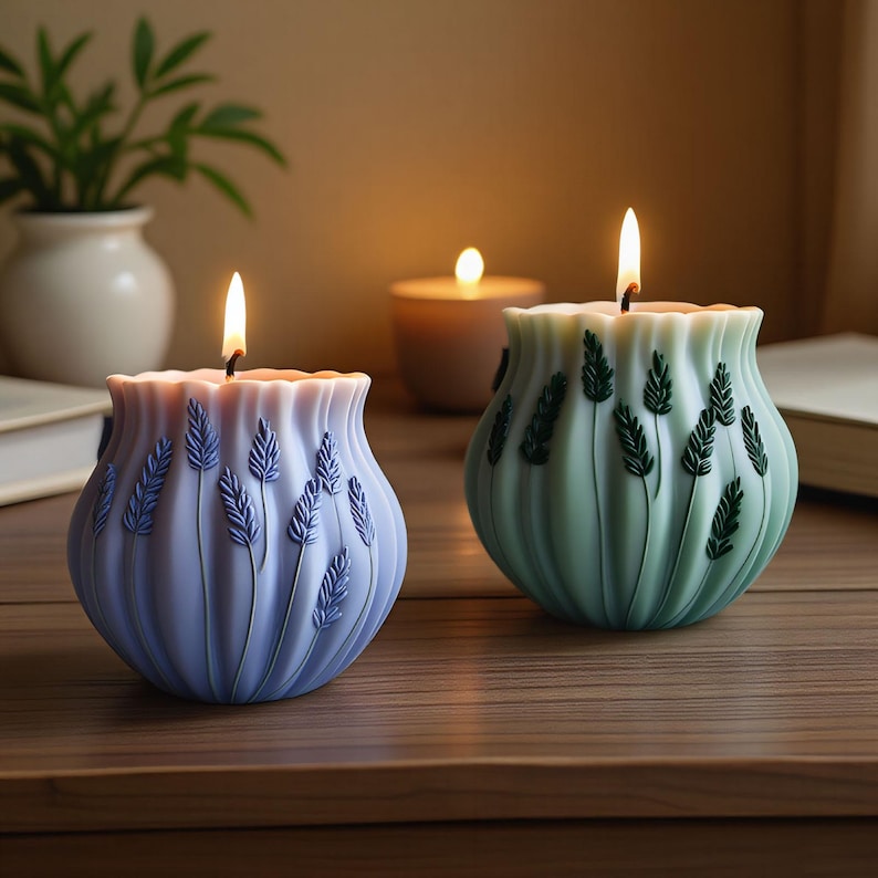 May include: Two lit, decorative candles with a floral design. One candle is light blue with lavender-colored accents, and the other is light green with dark green accents. Both candles have a wavy top and are on a wooden surface.