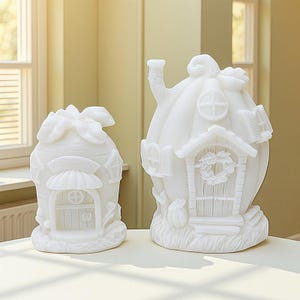May include: Two white ceramic decorative houses. The house on the left has a welcome sign above the door. The house on the right has a chimney, a wreath on the door, and a pumpkin on the side. Both houses have detailed architectural features.