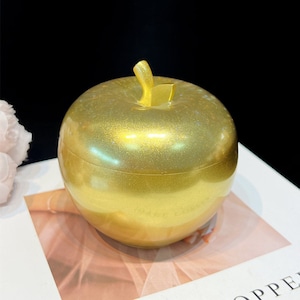 May include: A gold apple-shaped container with a shiny, glittery finish. The container is made of plastic and has a lid.