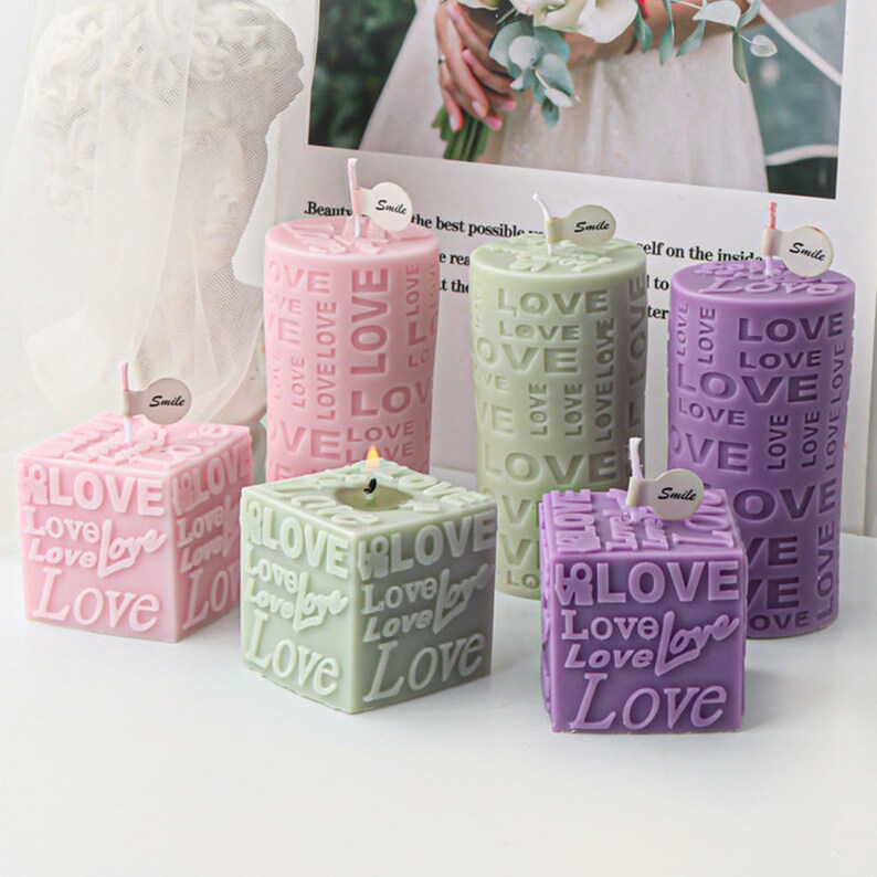 May include: Four candles in different shapes and sizes, all with the word "Love" embossed on them. The candles are pink, green, and purple.