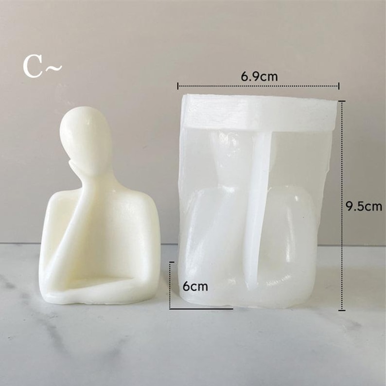 May include: A cream-colored candle in the shape of a person with their hand on their face, next to a clear plastic mold. The mold is rectangular, measuring 6 cm wide, 6.9 cm long, and 9.5 cm tall. The letter "C" is in the upper left corner.