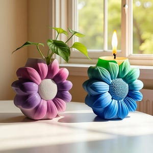 Könnte beinhalten: Zwei blütenförmige Dekorationsartikel. Einer ist eine Vase mit einer Pflanze, der andere eine Kerze. Die Vase ist lila und rosa mit einem weißen Zentrum. Die Kerze ist blau und grün mit einer brennenden gelben Flamme.