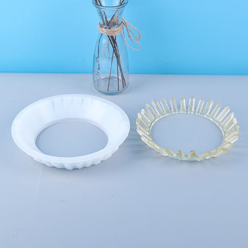 May include: Two white plastic plant saucers, one with a smooth surface and the other with a textured surface. The textured saucer has a raised edge.
