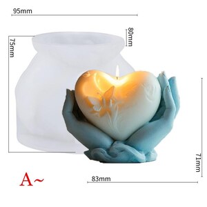 May include: A heart-shaped candle, approximately 3.2 inches wide and 2.8 inches tall, held by blue hands. The candle has a butterfly design and is lit. A clear mold, 3.7 inches wide and 3 inches tall, is also shown.