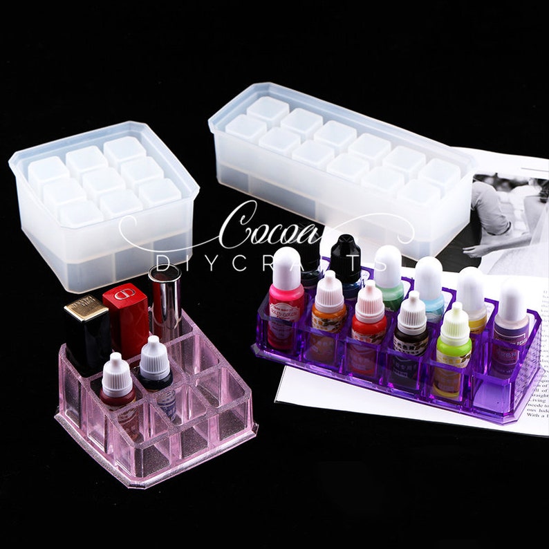 May include: Two clear silicone molds for making resin crafts. One mold is rectangular and has 12 square compartments. The other mold is square and has 9 square compartments. A purple plastic organizer with 12 compartments holds small bottles of liquid.
