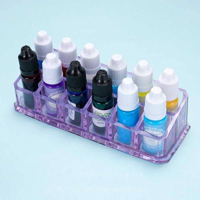 May include: A clear plastic organizer with 12 compartments for holding small bottles. The organizer is filled with bottles of various colors, including blue, green, purple, and yellow.