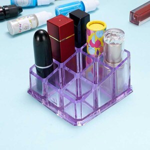 May include: A clear purple acrylic makeup organizer with 12 compartments. The organizer is filled with various makeup items, including lipsticks, lip gloss, and a lip balm.