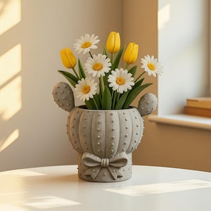 May include: A gray concrete cactus-shaped planter with a bow detail, filled with yellow tulips and white daisies. The planter has a textured surface with small, round bumps. The flowers have green stems and leaves.