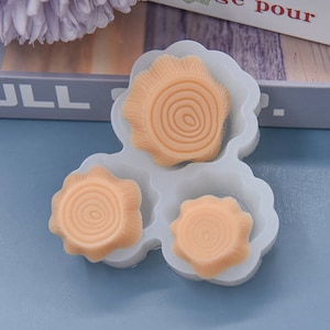 May include: A white silicone mold with three tree ring designs. The tree rings are a light orange color and have detailed concentric circles. The mold is on a blue surface.