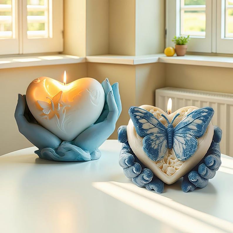 May include: Two heart-shaped candles with butterfly designs. One candle has an orange butterfly, the other a blue butterfly. Both candles are held by light blue hands. The candles are on a white table.