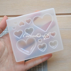 Puede incluir: Molde de silicona transparente con múltiples formas de corazón de diferentes tamaños. El molde es flexible y tiene una superficie lisa.