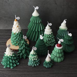 Puede incluir: Una colección de 11 velas de árbol de Navidad verdes y blancas. Las velas están hechas de cera y tienen una variedad de diseños, incluyendo un árbol de Navidad tradicional, un gorro de Papá Noel y un diseño en espiral.