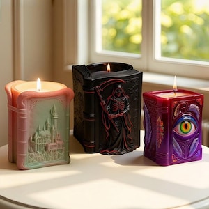 May include: Three lit candles in the shape of books. One is pink and green with a castle design, another is black with a Grim Reaper, and the third is purple with an eye design. The candles are on a white surface.