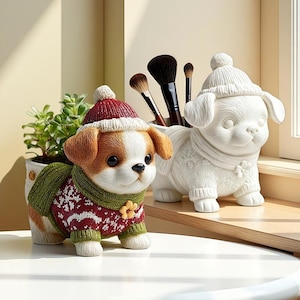 Puede incluir: Se muestran dos figuras decorativas de cachorros, una de color y otra blanca. El cachorro de color lleva un gorro rojo y blanco y un suéter verde con un diseño de copo de nieve. El cachorro blanco tiene un gorro y una bufanda a juego. Hay brochas de maquillaje en un recipiente.