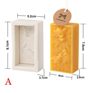 May include: A set of two bee-themed candle molds. The mold on the left is white and measures 5.2 cm wide, 9.1 cm tall, and 3.7 cm deep. The mold on the right is yellow and measures 4 cm wide, 7.8 cm tall, and 2.8 cm deep. The yellow mold has a label that says "Handmade".