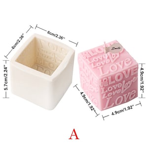 May include: A white silicone mold and a pink candle, both shaped like a cube. The candle is decorated with the word "Love" repeated in various sizes and orientations. The mold measures 5.7 inches by 6 inches. The candle measures 4.9 inches by 4.9 inches. The candle has a small tag that says "Smile".