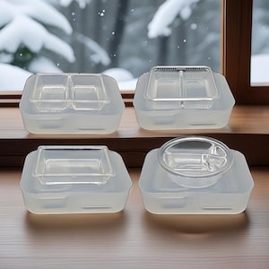Puede incluir: Se muestran cuatro recipientes transparentes y divididos para alimentos con bases de silicona a juego. Cada recipiente tiene un estilo diferente de bandeja transparente y dividida para alimentos. Los recipientes están sobre una superficie de madera con una escena nevada al aire libre en el fondo.