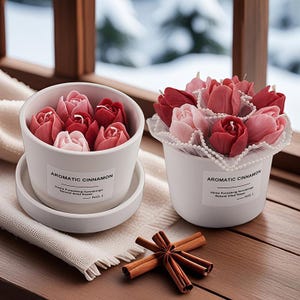 Könnte beinhalten: Zwei weiße Keramiktöpfe gefüllt mit tulpenförmigen Kerzen in Rot- und Rosatönen. Die Töpfe tragen Etiketten mit der Aufschrift "AROMATIC CINNAMON". Zimtstangen sind auf einer Holzoberfläche angeordnet.