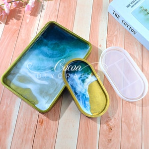 May include: Two resin trays with a blue and white marbled design. The larger tray is rectangular and the smaller tray is oval. Both trays have a gold rim.