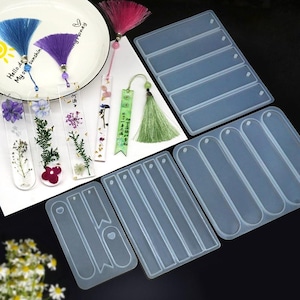 Può includere: Stampi per segnalibri in resina trasparente e segnalibri finiti con fiori secchi e nappe. Gli stampi sono rettangolari con un foro nella parte superiore per la nappa. I segnalibri finiti hanno nappe colorate.