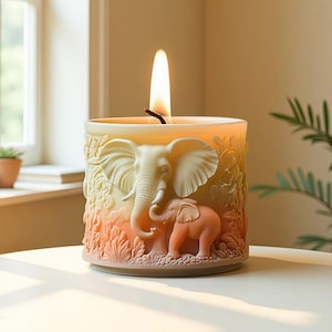 Pode incluir: Uma vela acesa em um recipiente cilíndrico com um design em relevo de elefantes. A vela tem um exterior creme com um gradiente de pêssego e verde claro. A vela está em uma superfície branca.