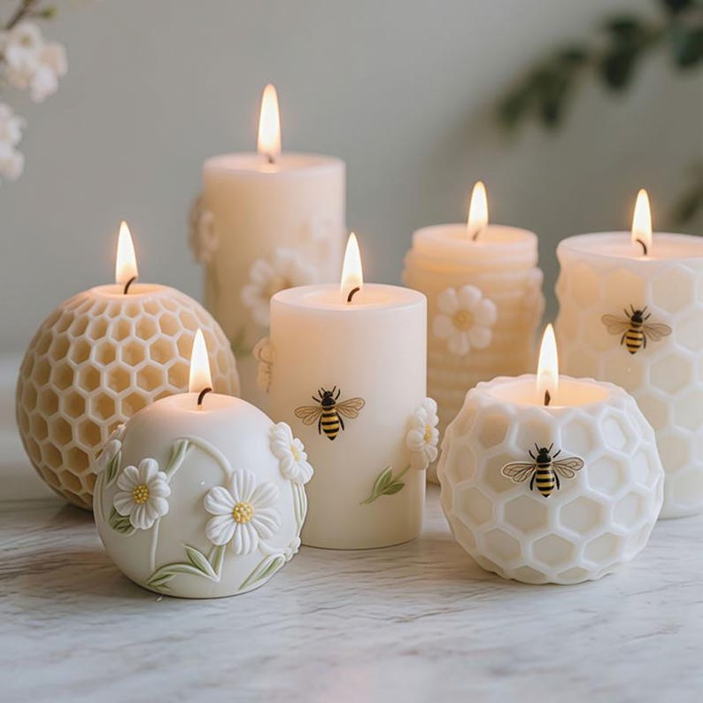 May include: A collection of lit, ivory-colored candles with various designs. Some candles feature honeycomb patterns, while others have floral or bee motifs. The candles are of different shapes and sizes, creating a warm and inviting ambiance.
