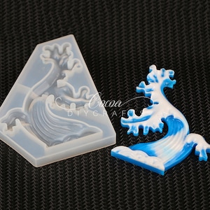May include: A clear silicone mold in a triangular shape with a wave design, next to a finished blue and white resin wave. The wave has a detailed, layered appearance, with a crest and flowing water. The text "Cocoa DIYCraft" is visible.