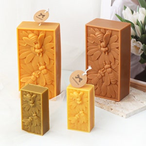 May include: Three rectangular beeswax candles with a honeybee and flower design. The candles are different sizes and are labeled "Handmade".