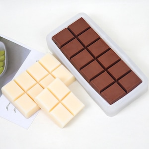 Peut inclure: Deux moules à barres chocolatées, l'un rempli de chocolat noir et l'autre de chocolat blanc. Les moules sont en silicone et ont une forme rectangulaire.