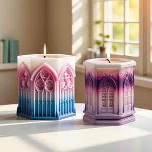 May include: Two lit, hexagonal candles with architectural designs. One candle has a white top that fades to pink and blue. The other candle is purple. Both candles have a gothic window design.