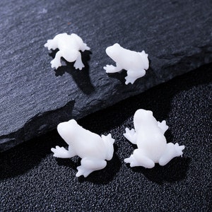 May include: Four white ceramic frog figurines. The frogs are in various poses, with their legs outstretched and their eyes closed.
